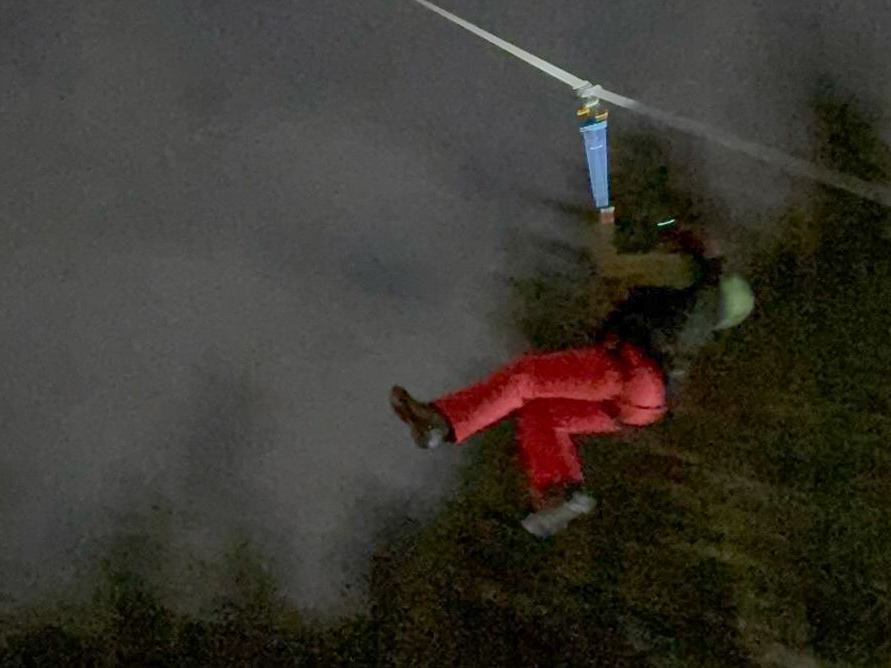 Osoba zjeżdżająca na linie w nocy, ubrana w czerwoną odzież i kask ochronny.