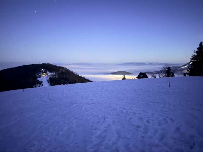 Widok na ośnieżony krajobraz górski o poranku, z mgłą pokrywającą doliny.